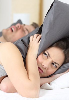 Woman pulling a pillow over her head as husband snores